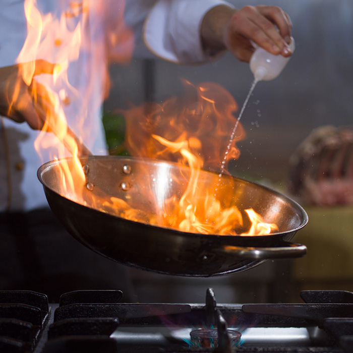 A chef adds liquid to a burning pan.