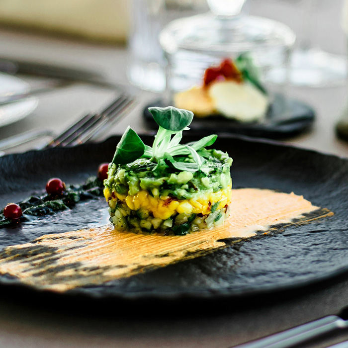 A green appetizer sitting in orange sauce on a black plate.